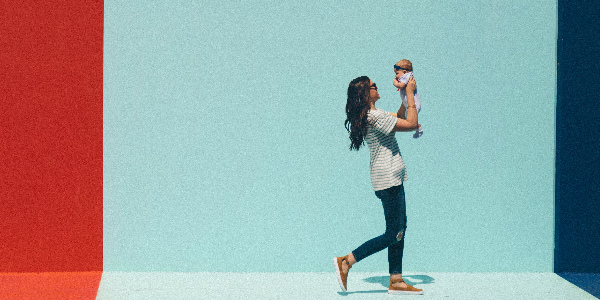 mother joyously carries her baby in front of a red, white and blue painted wall, representing the journey of maternity benefits for employees